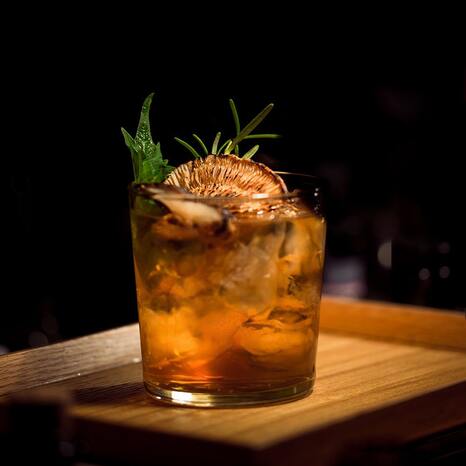 Das Bild zeigt einen Whiskey in einem Glas. Er sieht orange aus und ist mit Kräutern garniert.