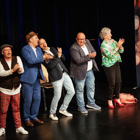 Fünf Personen stehen auf der Bühne. Sie klatschen und singen. Auf einem Banner steht "Schwäbische Comedy".