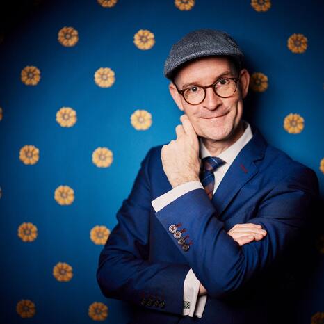 Portraitaufnahme von Pit Hartling. Er trägt eine Schiebermütze und einen Anzug.